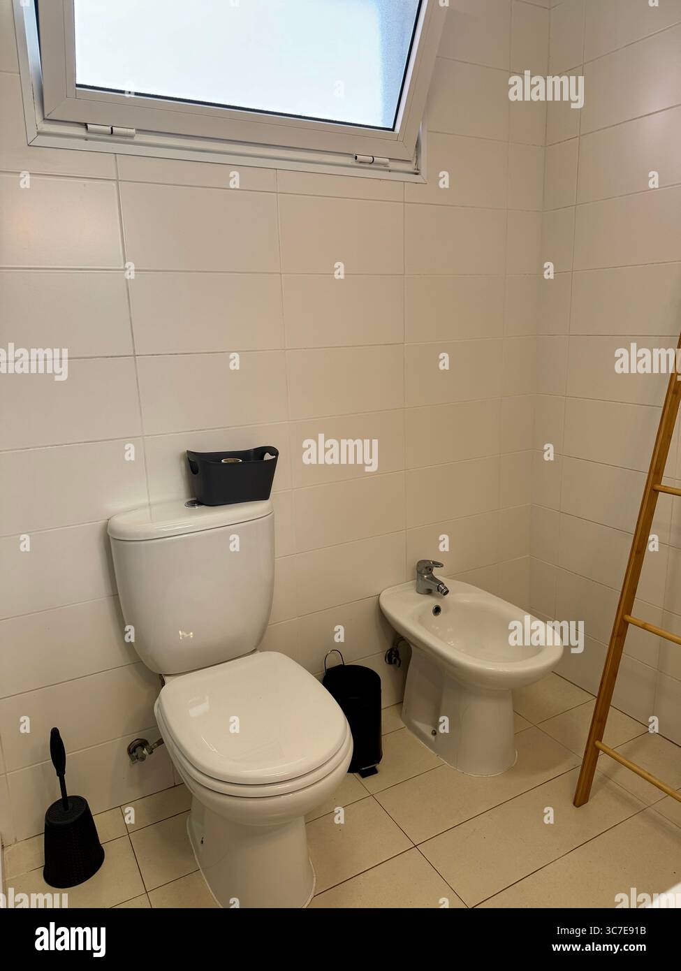 modern, clean bathroom with white tiles, a shower cabin, toilet, bidet, sink, and storage shelves. - Smartphone Captured Stock Image