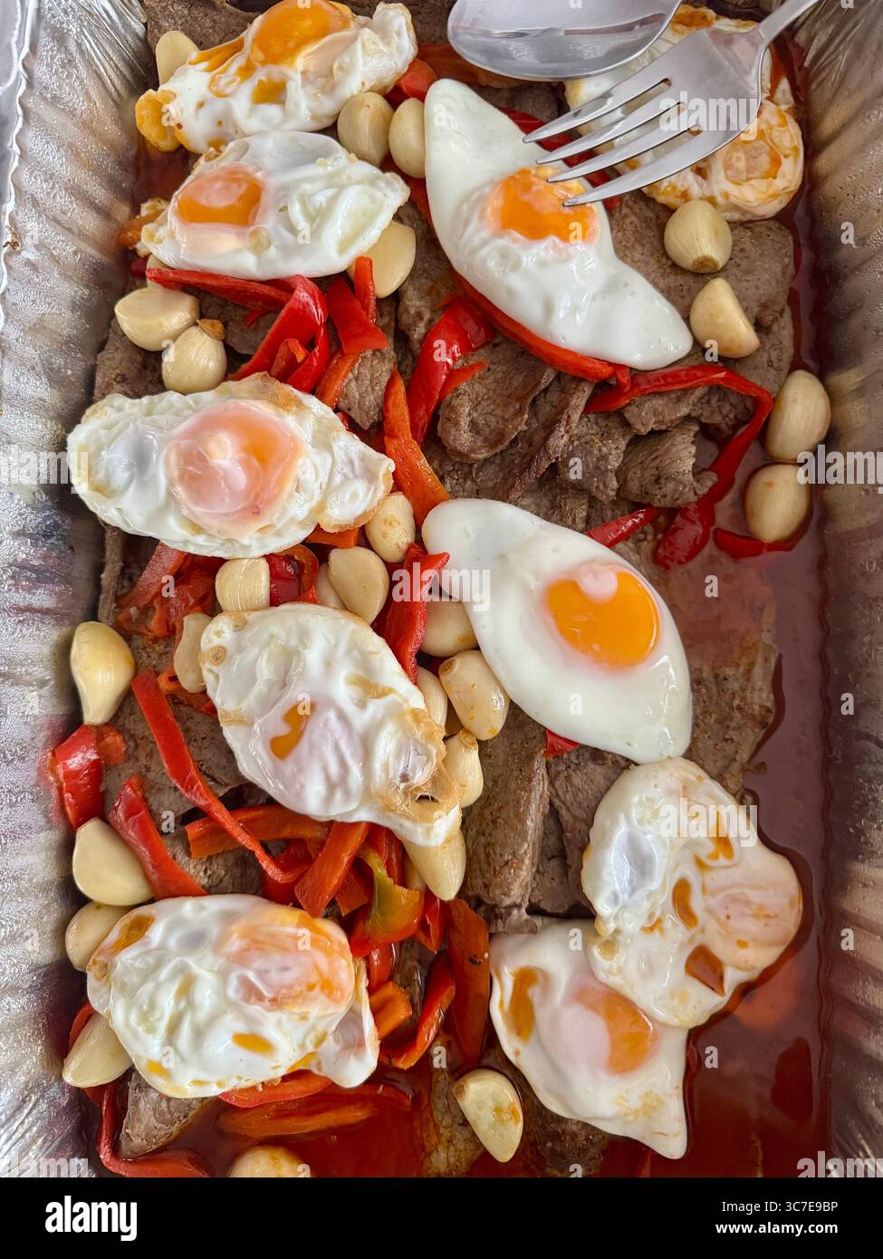 Traditional Portuguese takeaway meal featuring fried eggs, peppers, and beef strips in a food container. - Smartphone Captured Stock Image