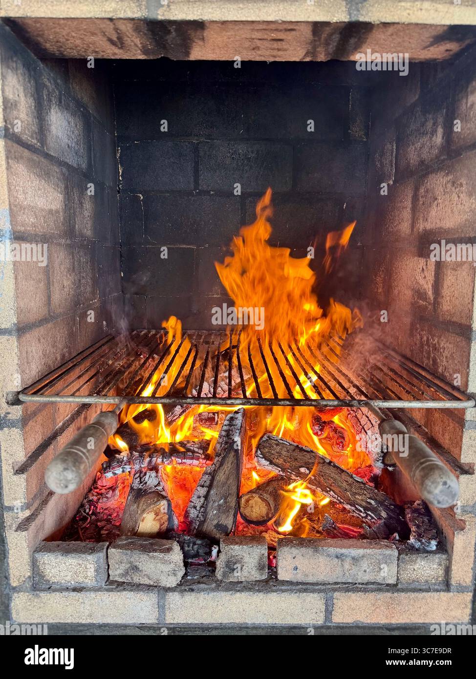 Flames rising on a barbecue grill fueled by burning wood, ready for outdoor cooking. - Smartphone Captured Stock Image