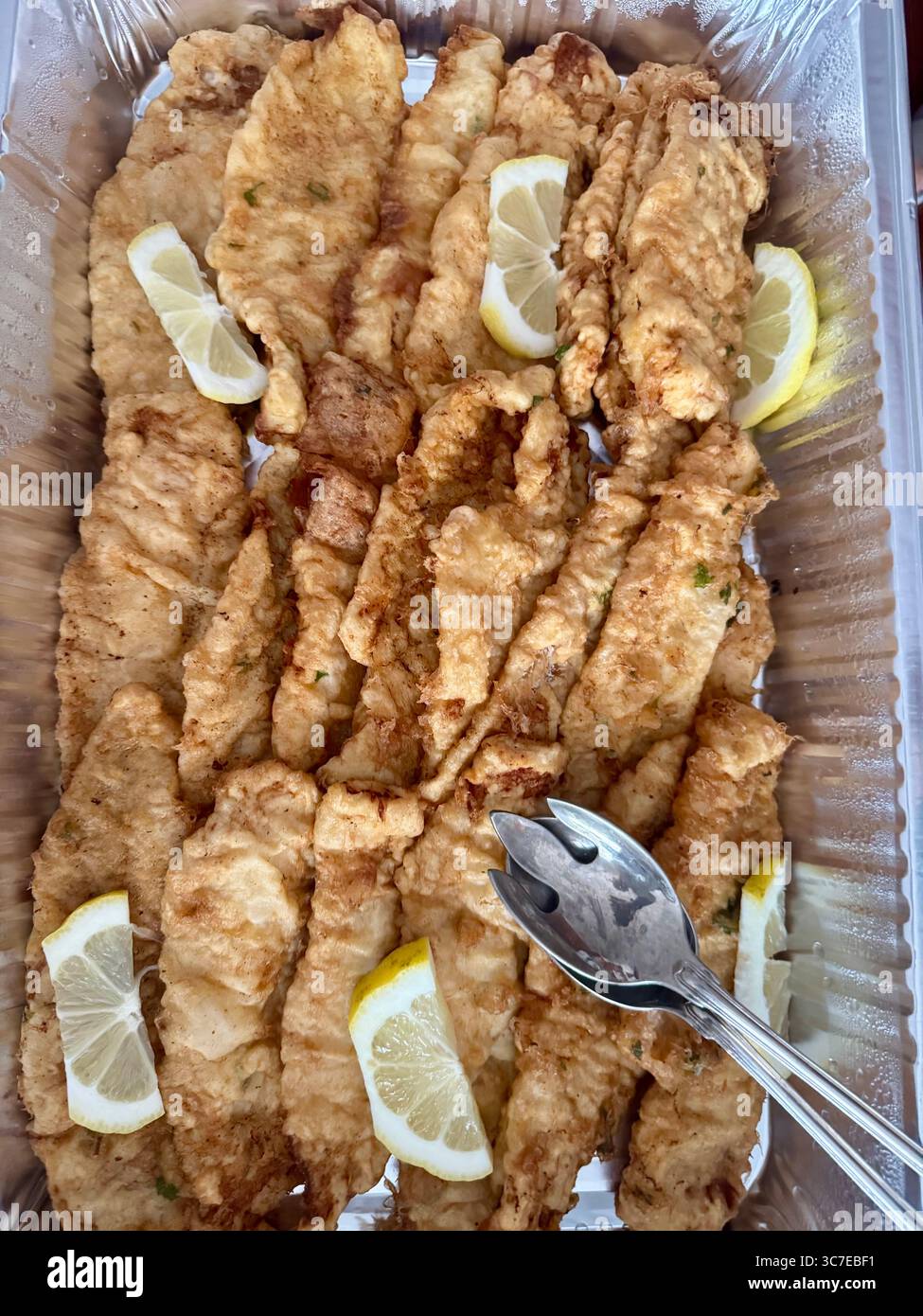Portuguese takeaway meal featuring crispy fried fish fillets garnished with lemon slices in a food container. - Smartphone Captured Stock Image