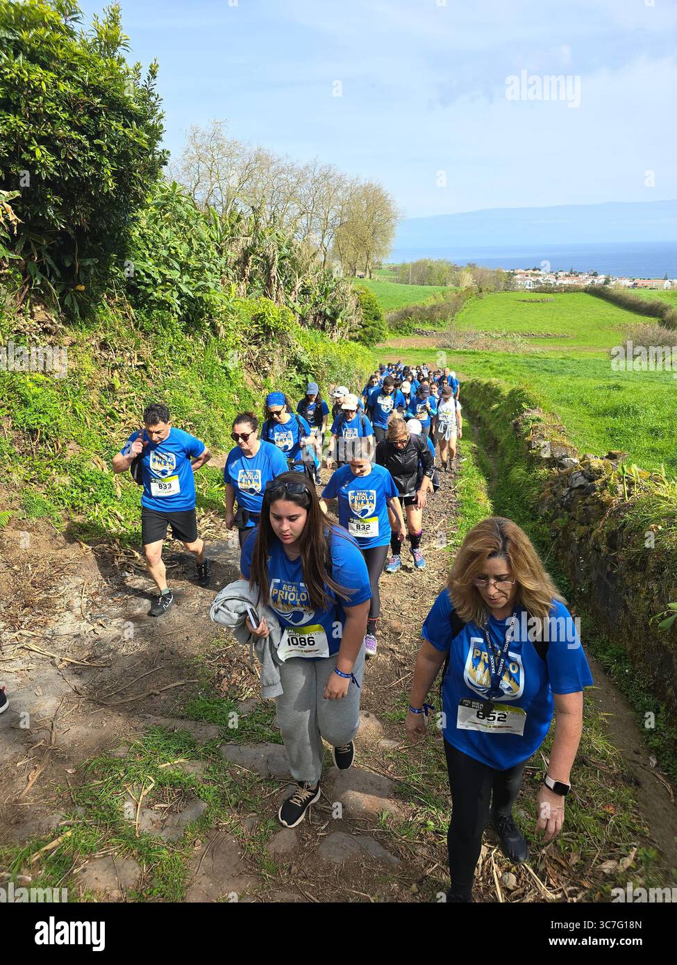 Participants running and hiking through lush forest trails and historic town streets during the Trail Real Priolo event in São Miguel Island, Azores, - Smartphone Captured Stock Image
