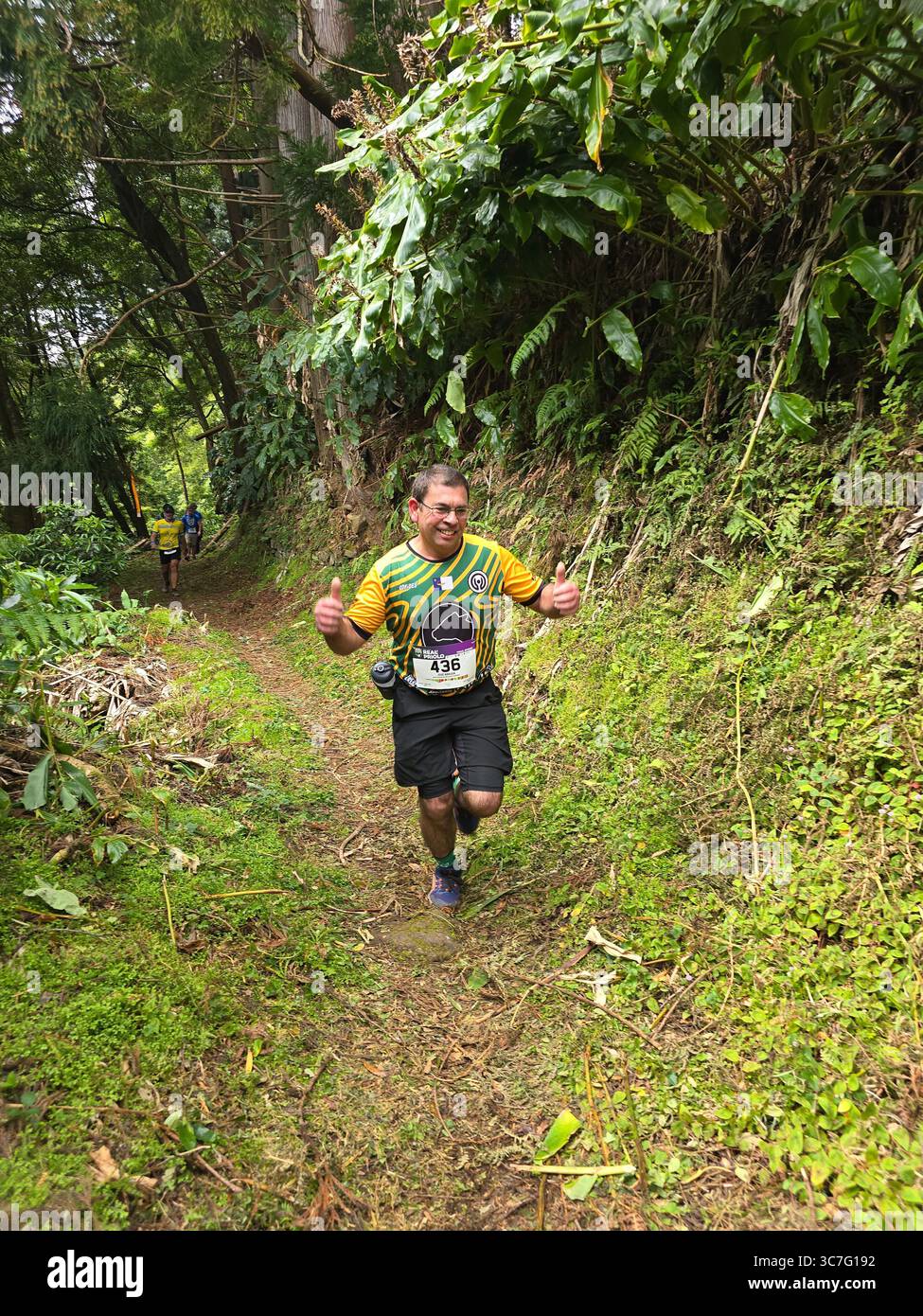 Participants running and hiking through lush forest trails and historic town streets during the Trail Real Priolo event in São Miguel Island, Azores, - Smartphone Captured Stock Image