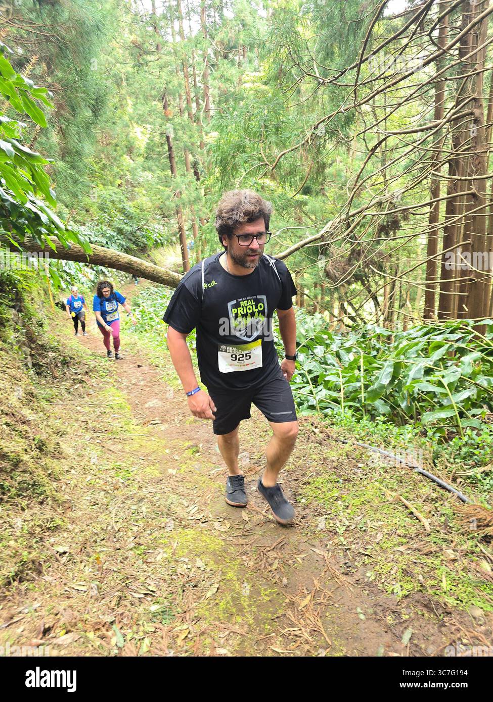 Participants running and hiking through lush forest trails and historic town streets during the Trail Real Priolo event in São Miguel Island, Azores, - Smartphone Captured Stock Image
