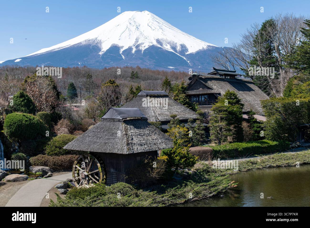 Traditional buildings with thatched roof in Oshino Village, Japan with in the background active stratovolcano Mt. Fuji with snow covered symmetrical c Stock Photo