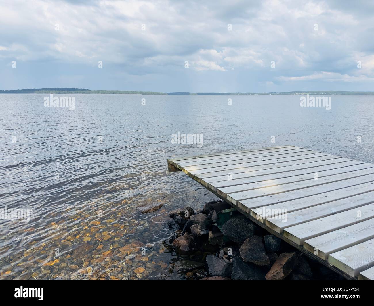Wooden dock on a calm lake under a cloudy, overcast sky. - Smartphone Captured Stock Image