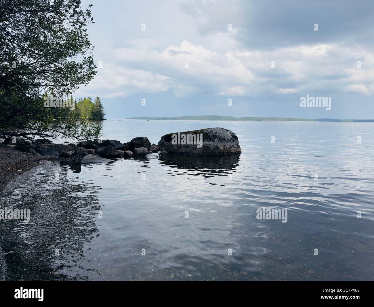 Calm lake with rocks in the foreground under a cloudy sky - Smartphone Captured Stock Image