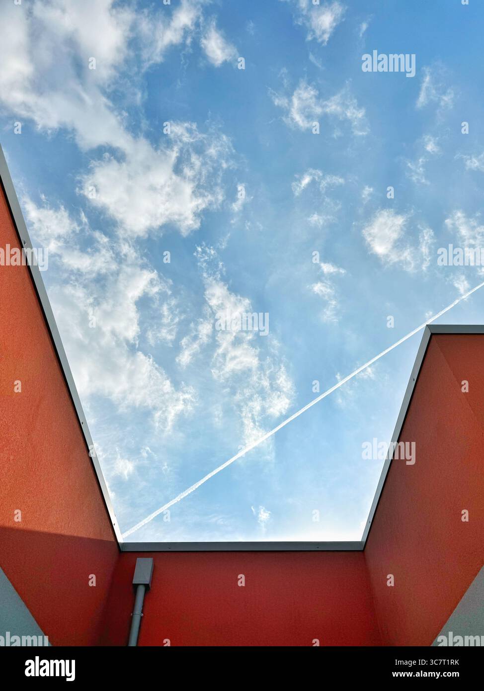 Abstract of terracotta walls against a blue sky with a diagonal vapour trail making a geometric pattern - Smartphone Captured Stock Image
