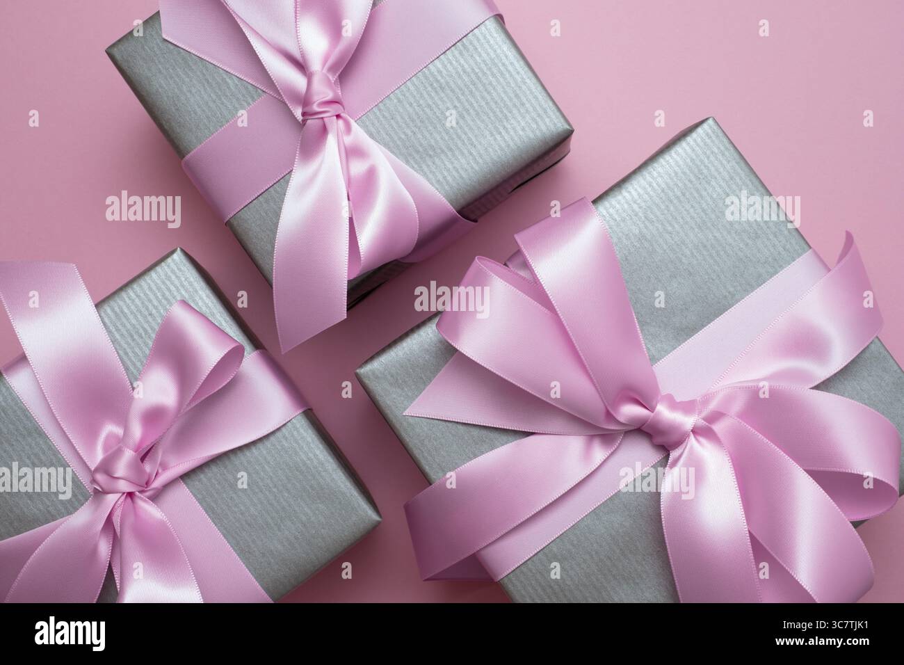 Silver gray gift boxes with pink satin bows on pink background. Surprise present. Stock Photo