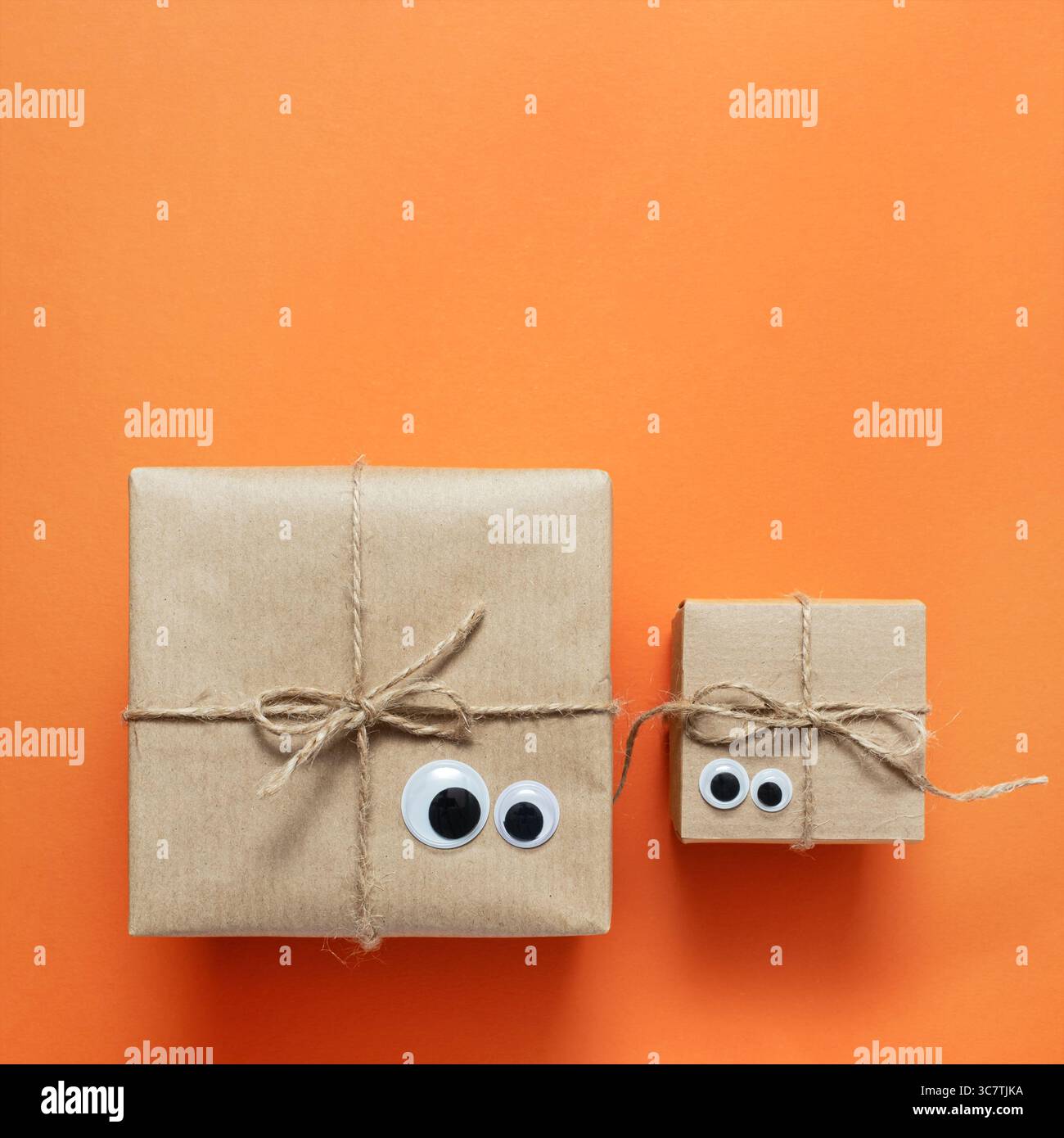 Card with brown craft gift boxes with eyes on orange background. Space for your text, square. Stock Photo
