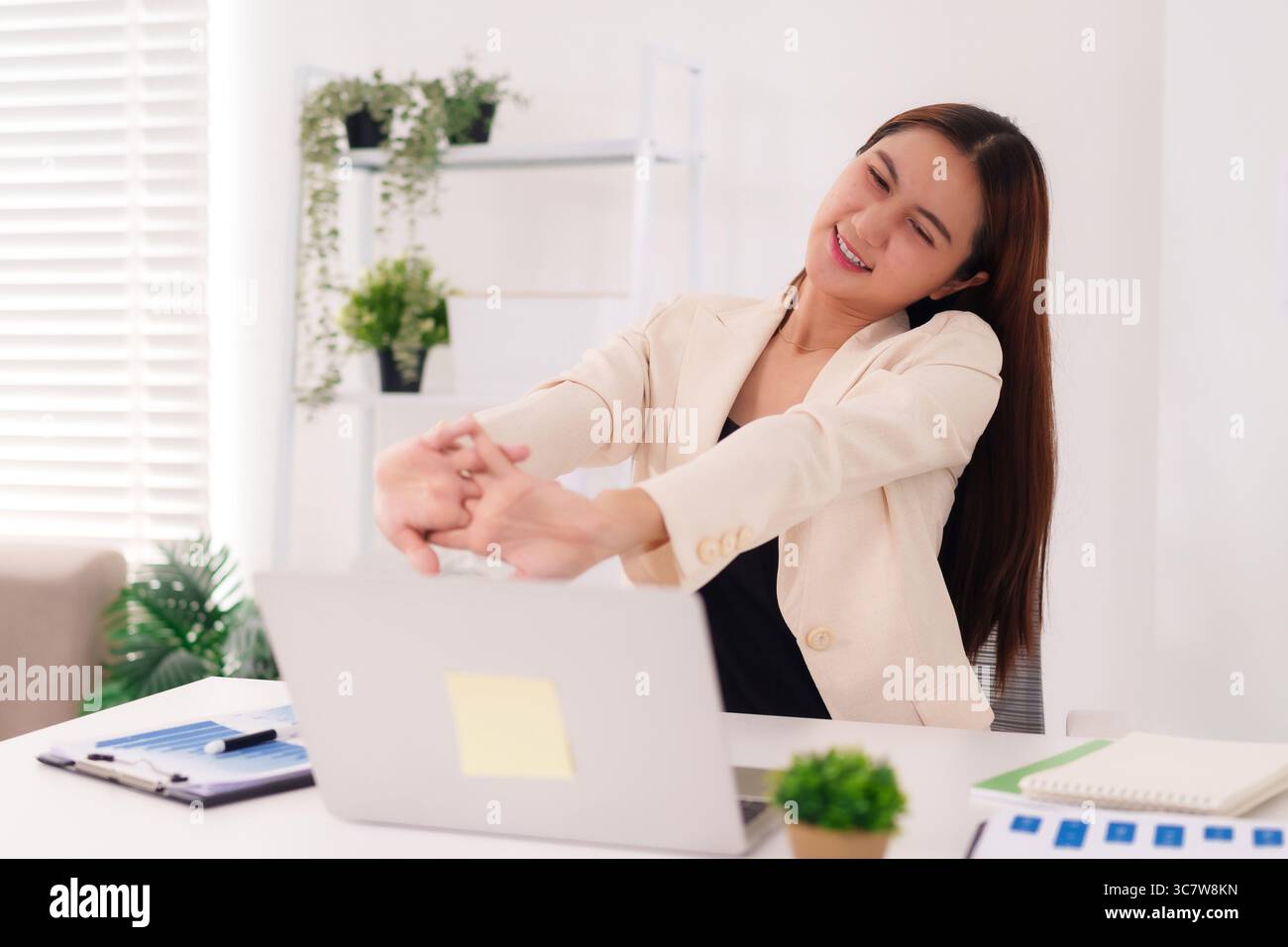 Stretches When Using A Computer Asian adult woman stretches at bright office desk during work break ...
