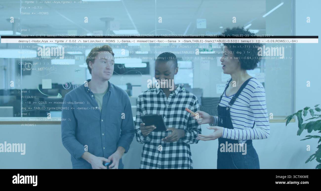 Discussing three software developers examining code on tablet in office, with coding wall and plant Stock Photo