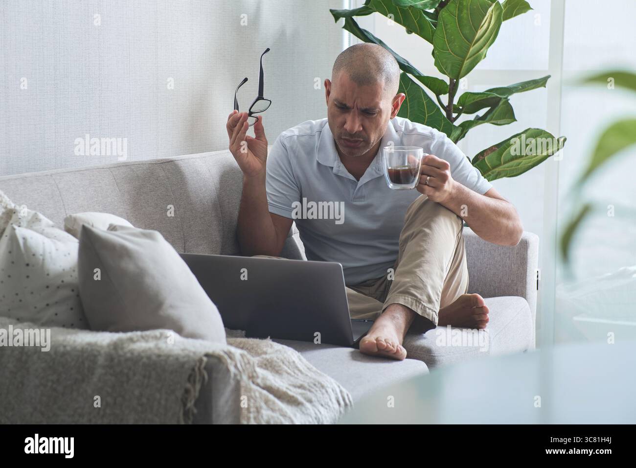 Concentrated businessman drinking coffee and using laptop while working remotely at home Stock Photo
