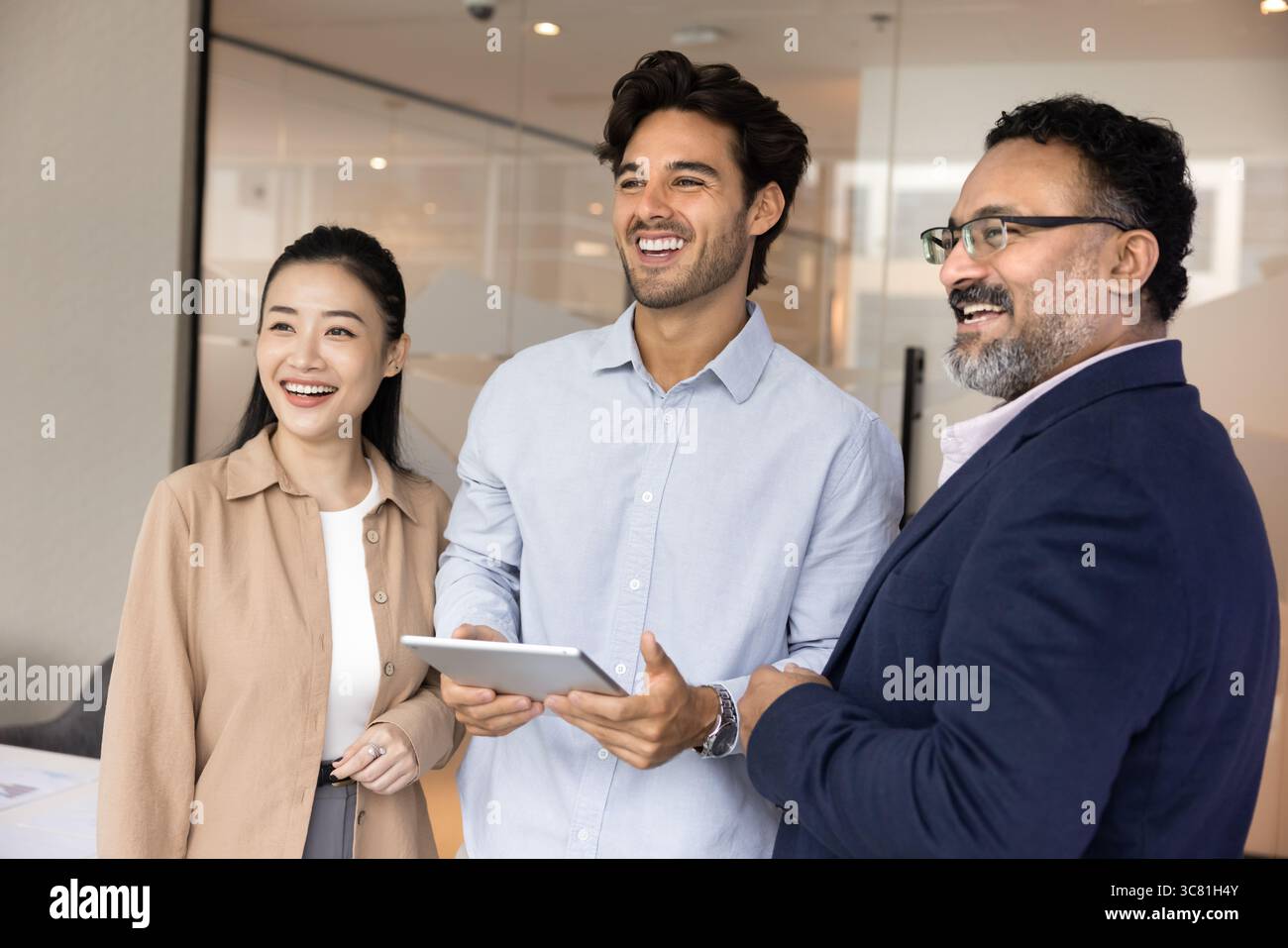Successful smiling diverse multiethnic business partners looking aside using tablet Stock Photo