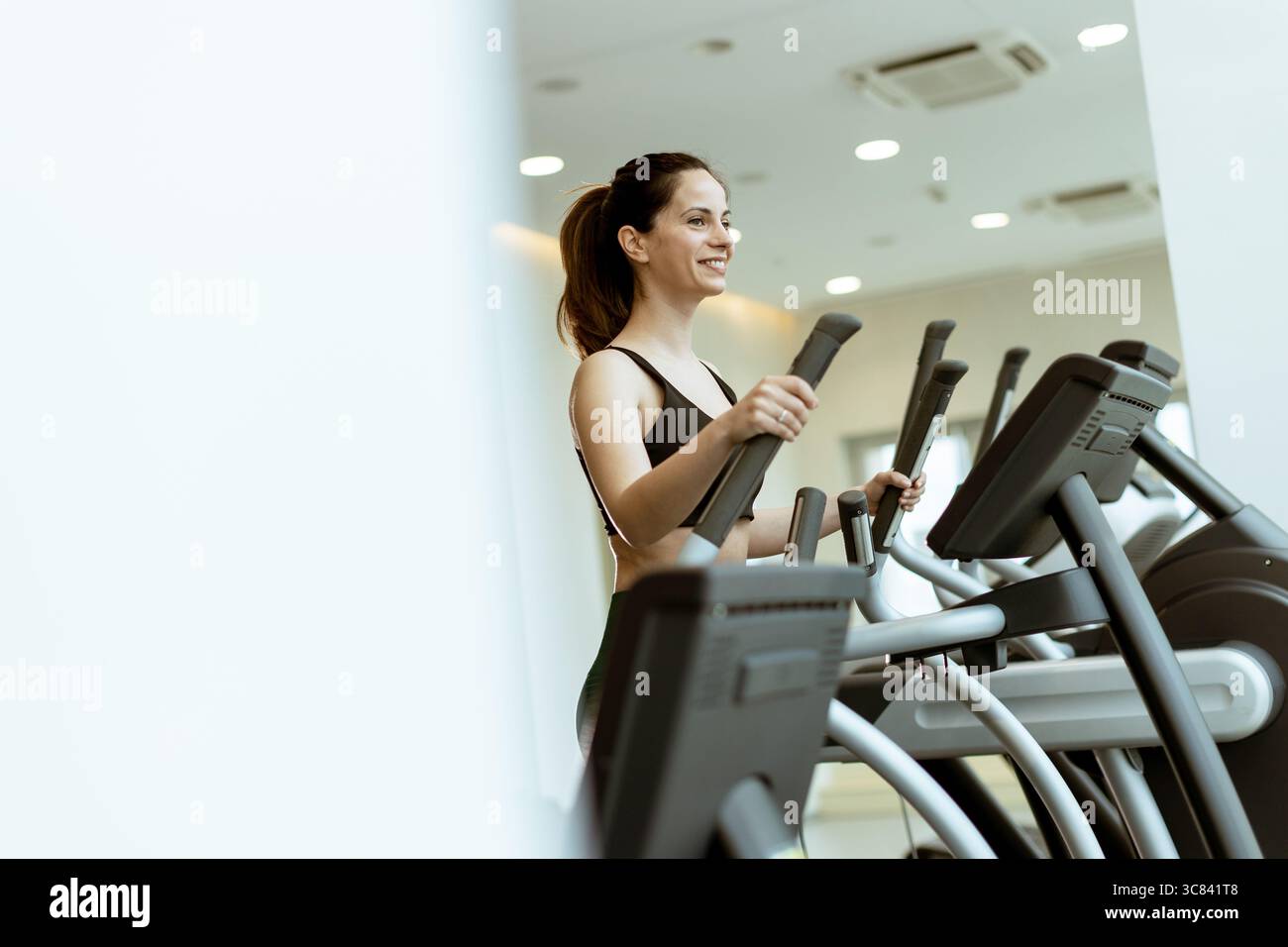 A fitness enthusiast powers through her morning elliptical workout, energized by modern gym gear and bright lighting. Stock Photo
