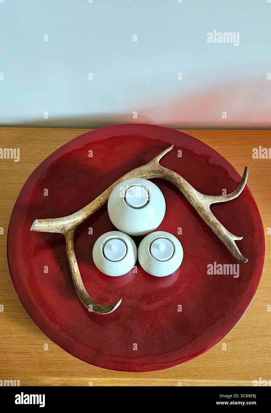 Top-down view of a decorative red tray featuring a deer antler and three minimalist white tea light candle holders, set on a wooden surface. - Smartphone Captured Stock Image