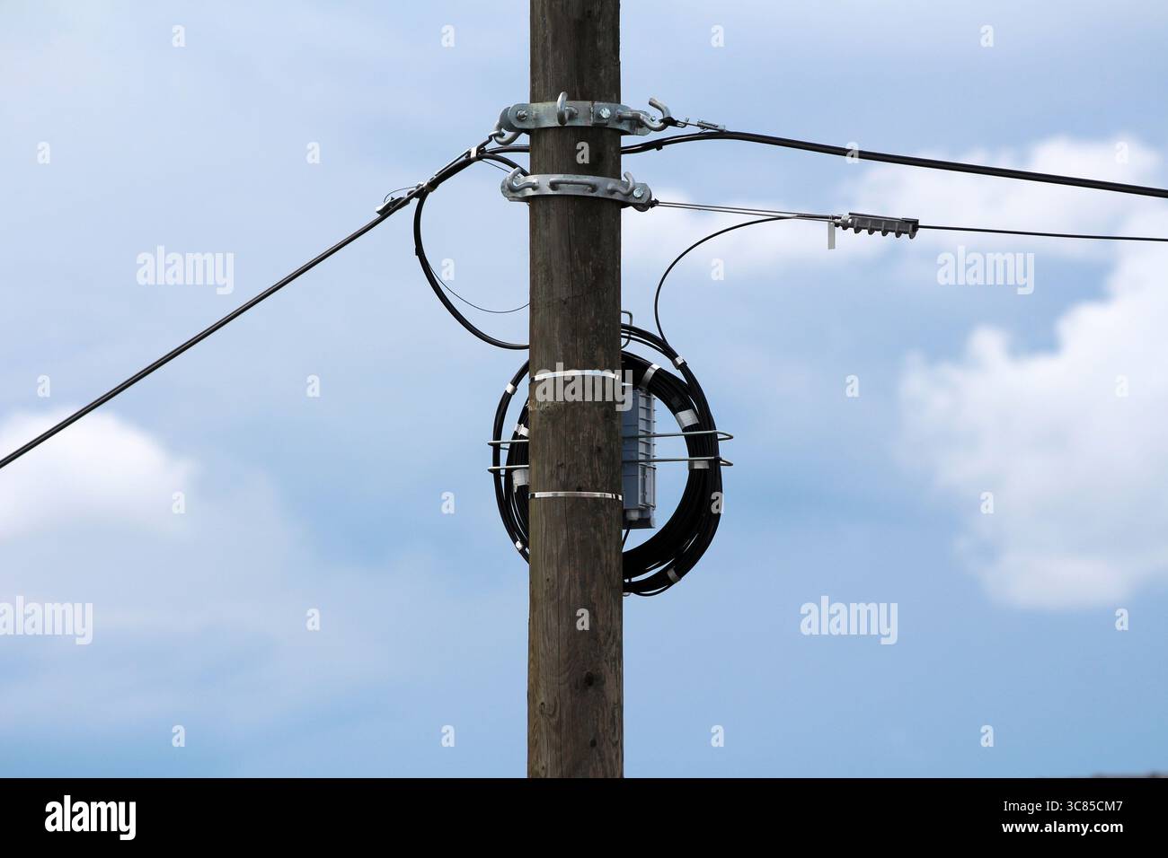 A utility pole with a mounted fiber optic splice enclosure and a coiled drop cable facilitates broadband or telecommunication connections in overhead Stock Photo