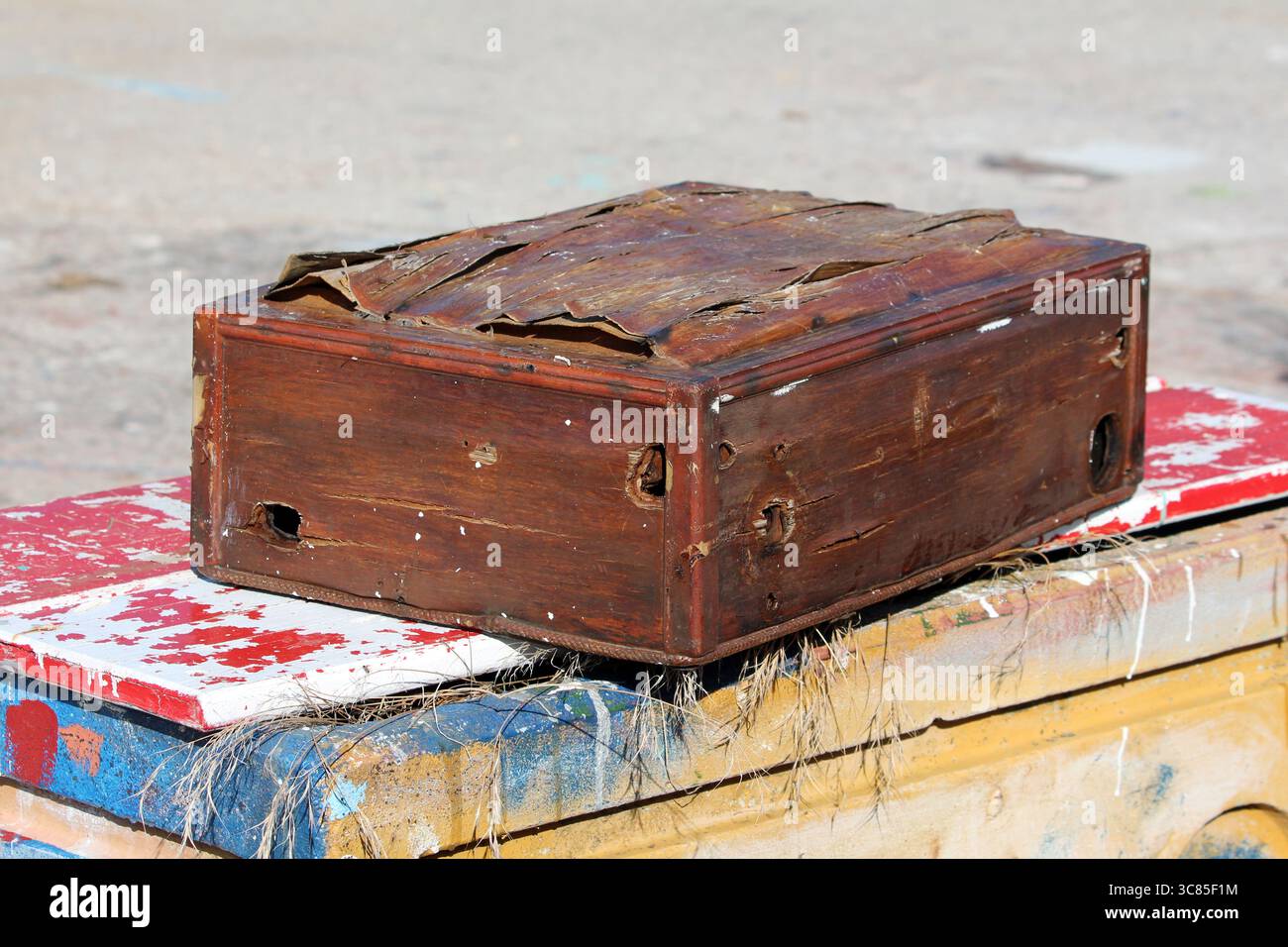 A battered, antique-style wooden box with warped panels, peeling surfaces, and visible distress marks, placed outdoors on colorful, paint-chipped Stock Photo