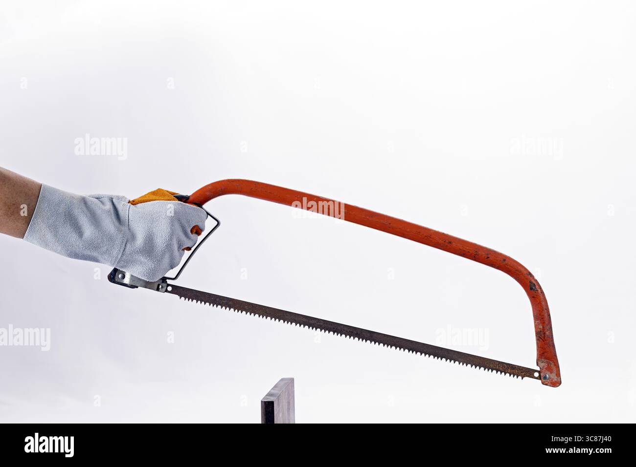 A gloved hand holds rusty hacksaw, poised to cut piece of wood, against plain white background. image captures sense of focus and craftsmanship Stock Photo