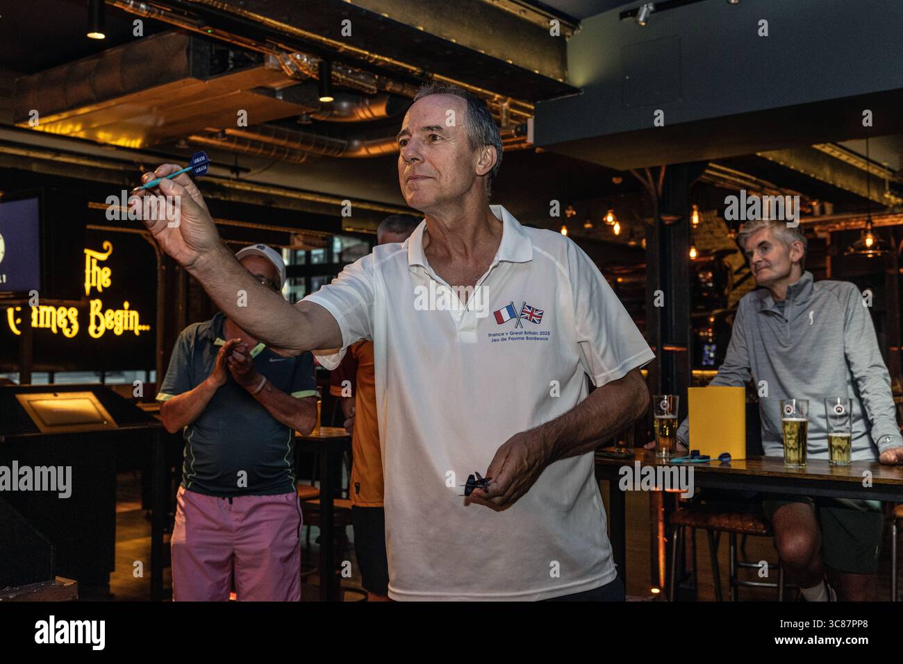 Man throwing darts at a dart bar, focusing on precision and skill during a casual game night in a lively pub atmosphere. Stock Photo