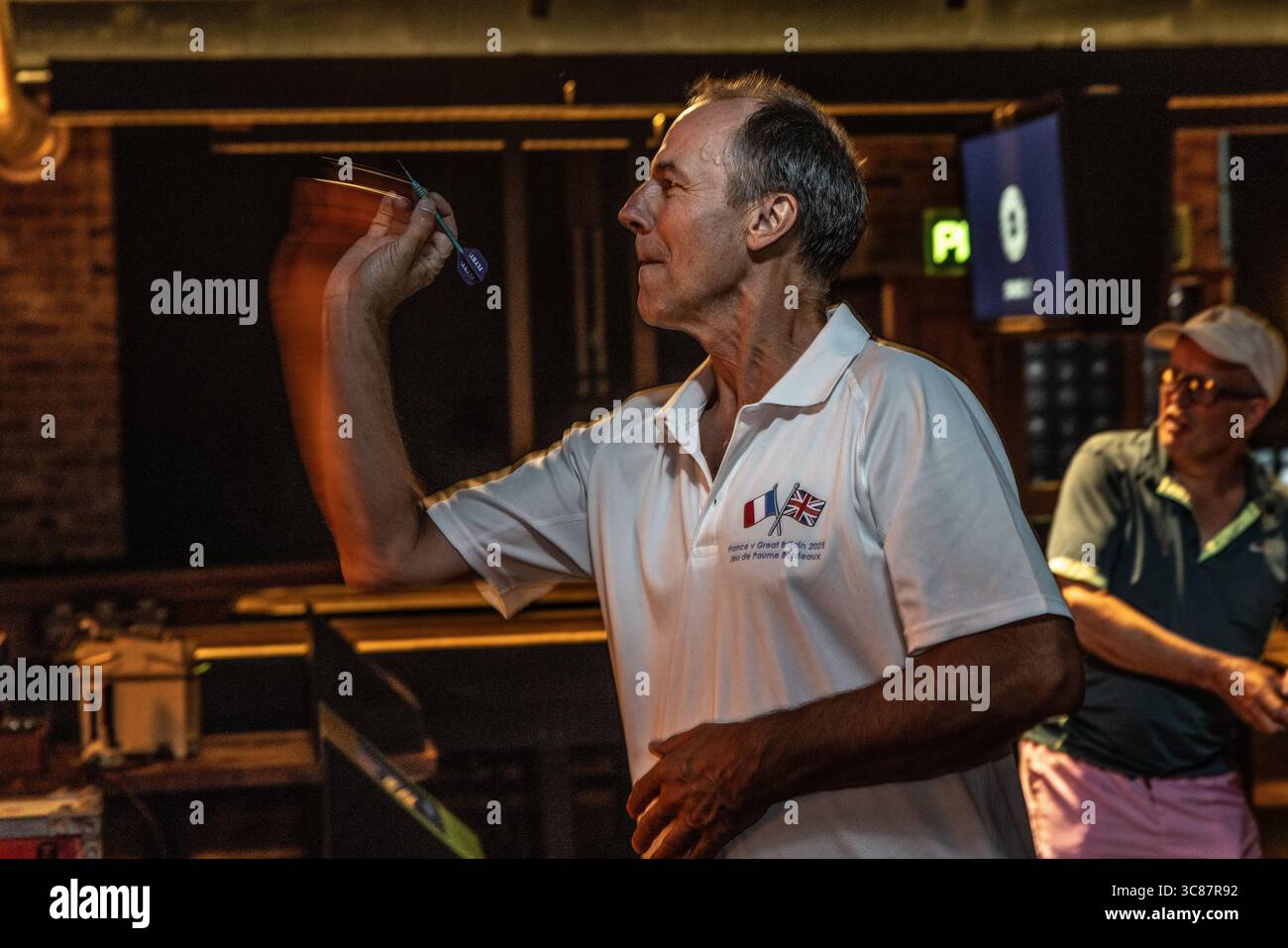 Man throwing darts at a dart bar, focusing on precision and skill during a casual game night in a lively pub atmosphere. Stock Photo