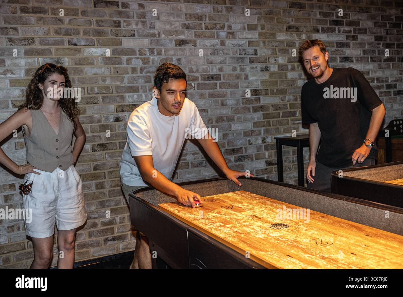 Young people enjoying a game of shuffleboard together, showcasing social leisure and friendly competition in a relaxed indoor setting. Stock Photo
