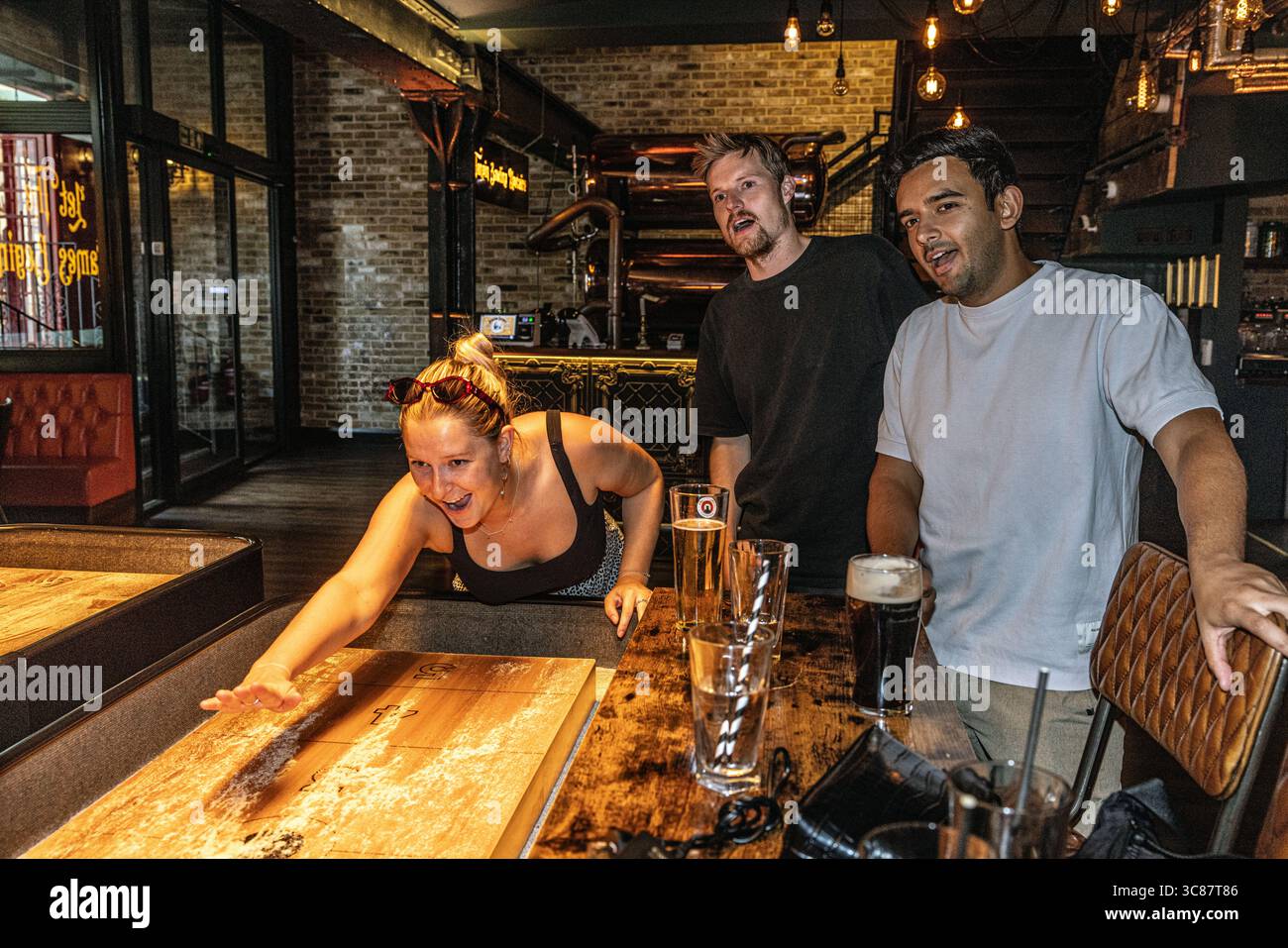 Young people enjoying a game of shuffleboard together, showcasing social leisure and friendly competition in a relaxed indoor setting. Stock Photo