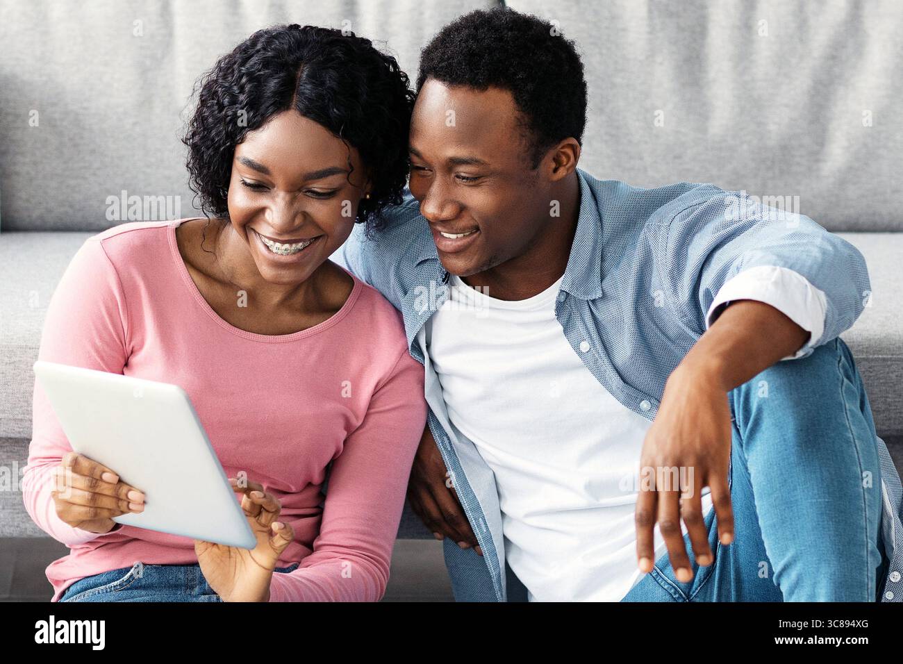 Smiling black couple with cleaning tools resting, using digital tablet Stock Photo