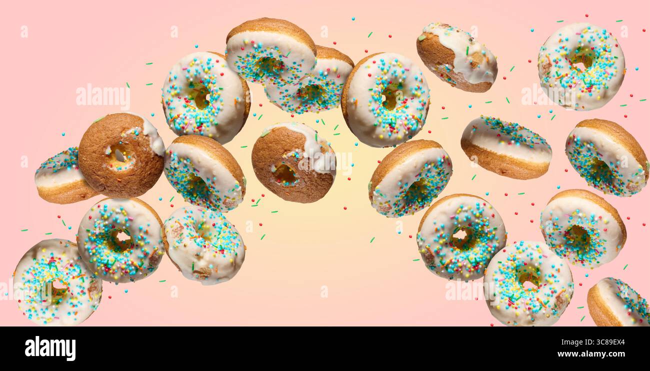 Multiple white glazed donuts with colorful sprinkles falling or flying in a curved path on a gradient pink and yellow background. Stock Photo