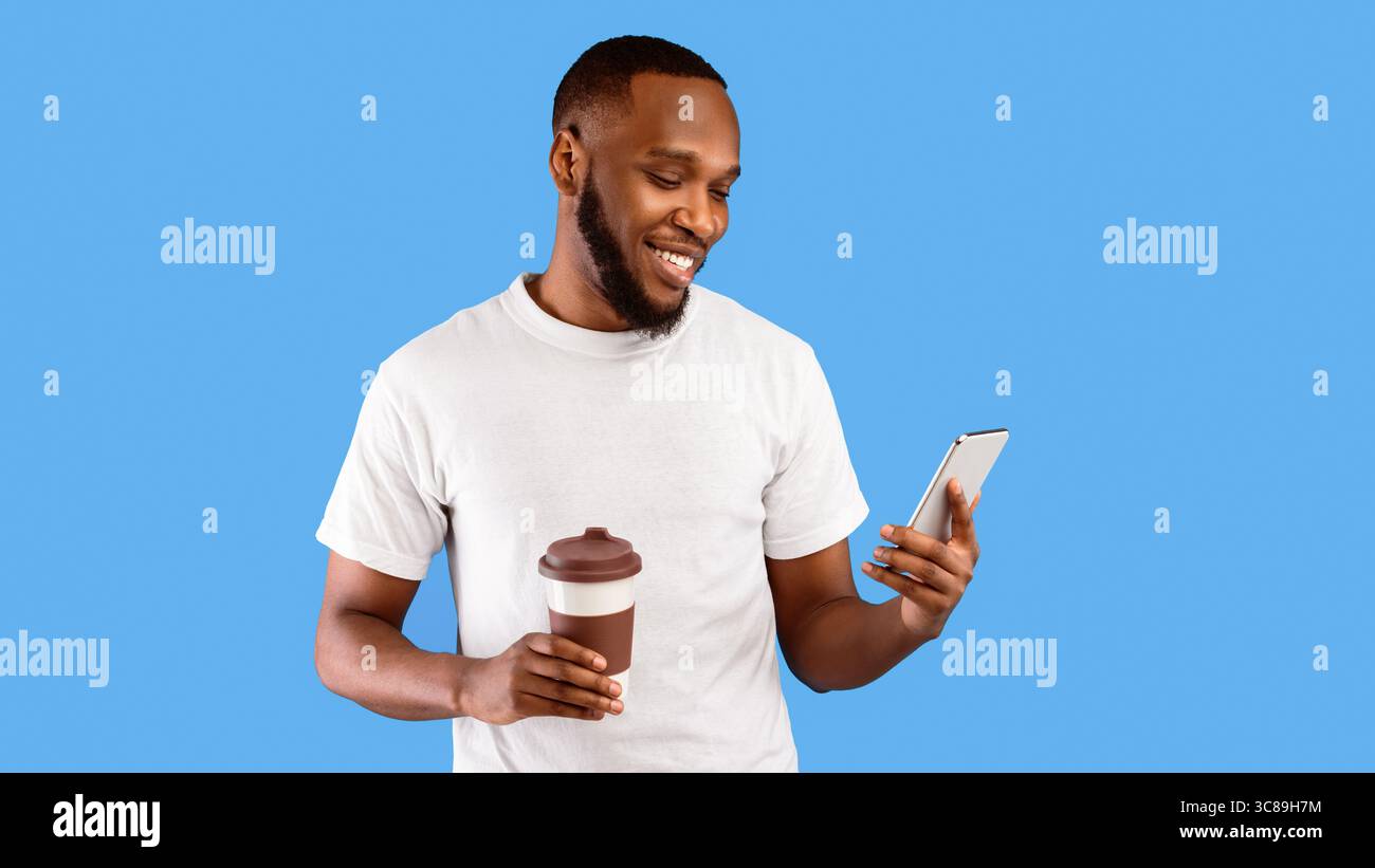 Black Guy Using Phone Holding Paper Coffee Cup, Blue Background Stock Photo