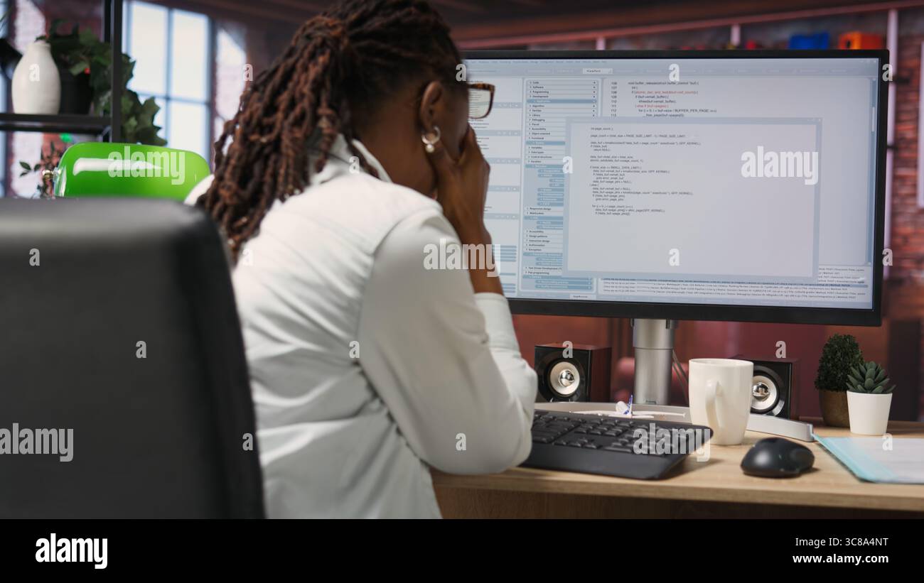 Woman feeling worried while looking at UI on PC screen, having trouble executing programming code. Anxious IT developer concerned by errors popping up while testing code in apartment, camera B Stock Photo