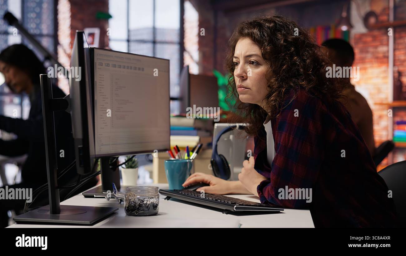 Happy employee using programming languages on PC in IT startup office to build applications. Cheerful IT expert using computer in software development agency to code, camera B Stock Photo