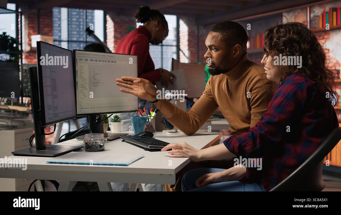Team of IT specialists using programming languages on PC in startup office to build applications. Teamworking colleagues using computer in software development agency to code, camera A Stock Photo