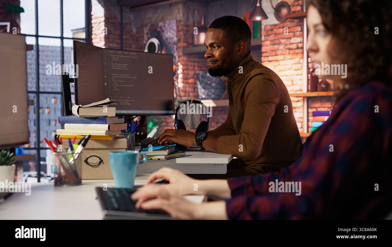 Irked man punching startup office desk in frustration struggling to fix application errors. Upset programmer annoyed by computer bugs while coding in software development agency, camera B Stock Photo