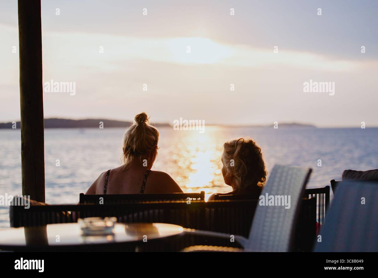 Silhouettes of two unrecognizable middle-aged ladies chatting while sitting on chairs near sea beach at  sunset. Concept of senior leisure. Friends on Stock Photo