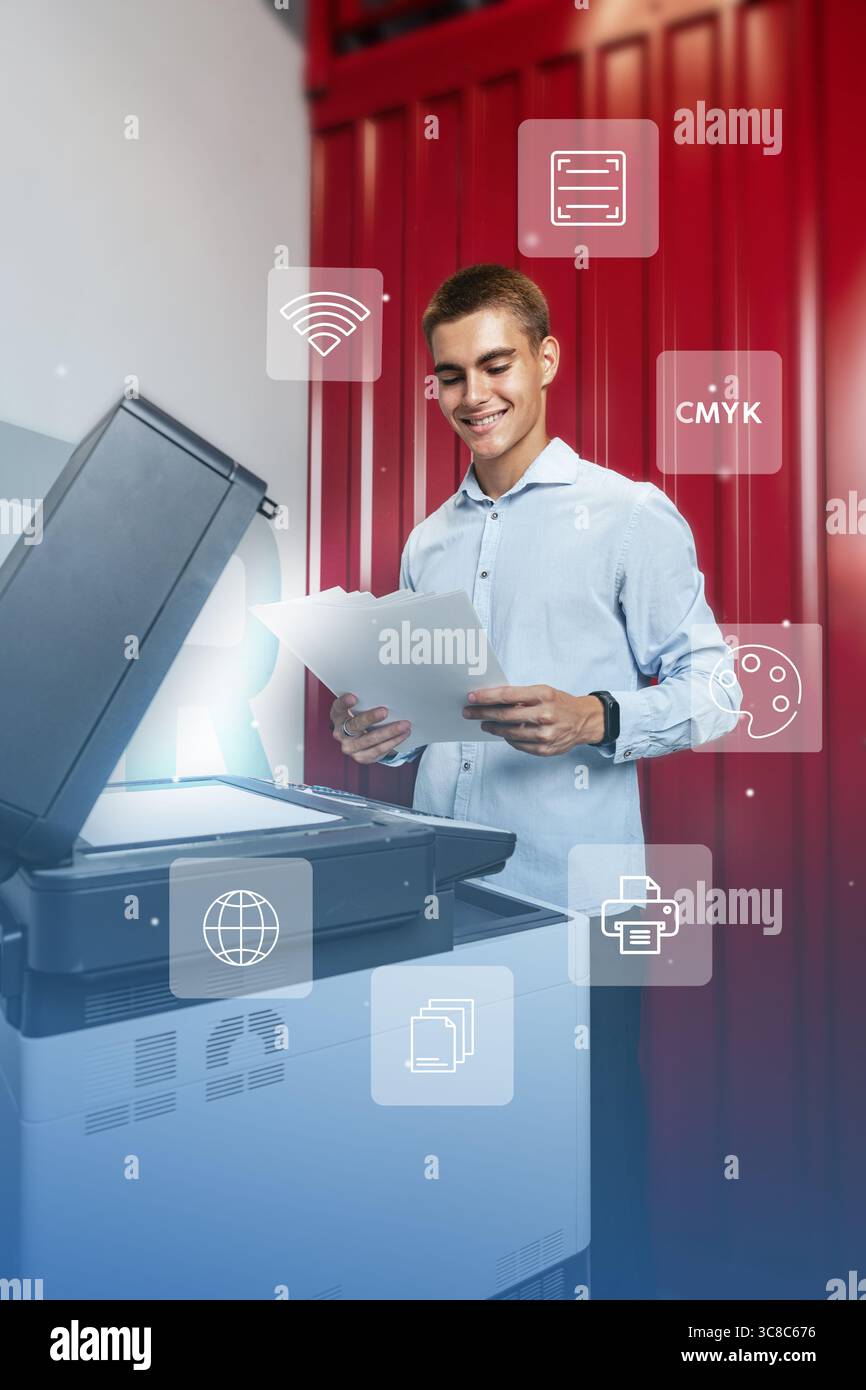 Young man smiling while using a multifunction printer for printing documents in a modern workspace Stock Photo