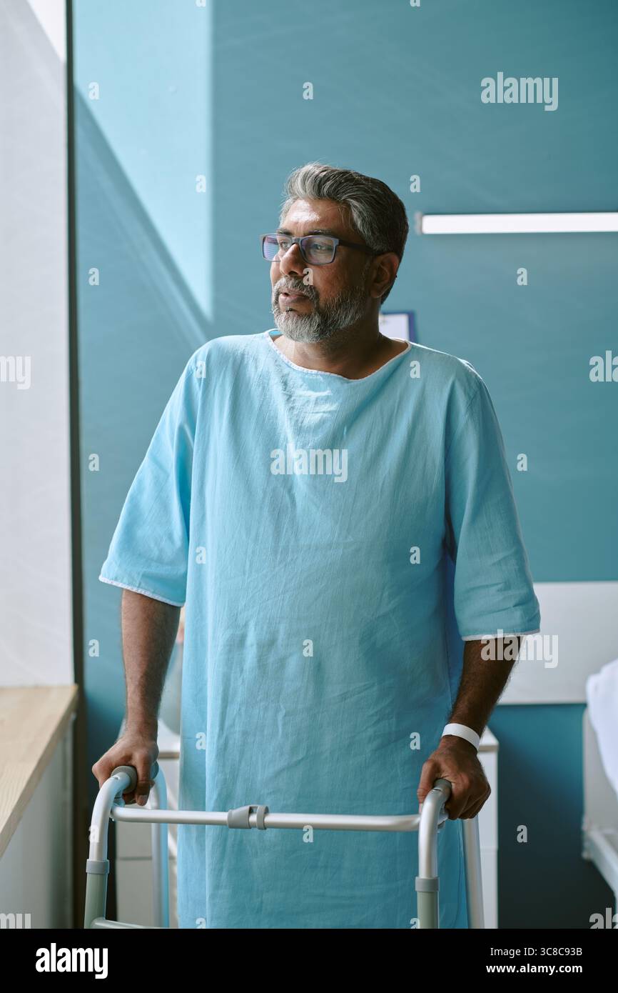 Middle Aged Biracial Man Standing by Window Using Walker during Recovery Stock Photo