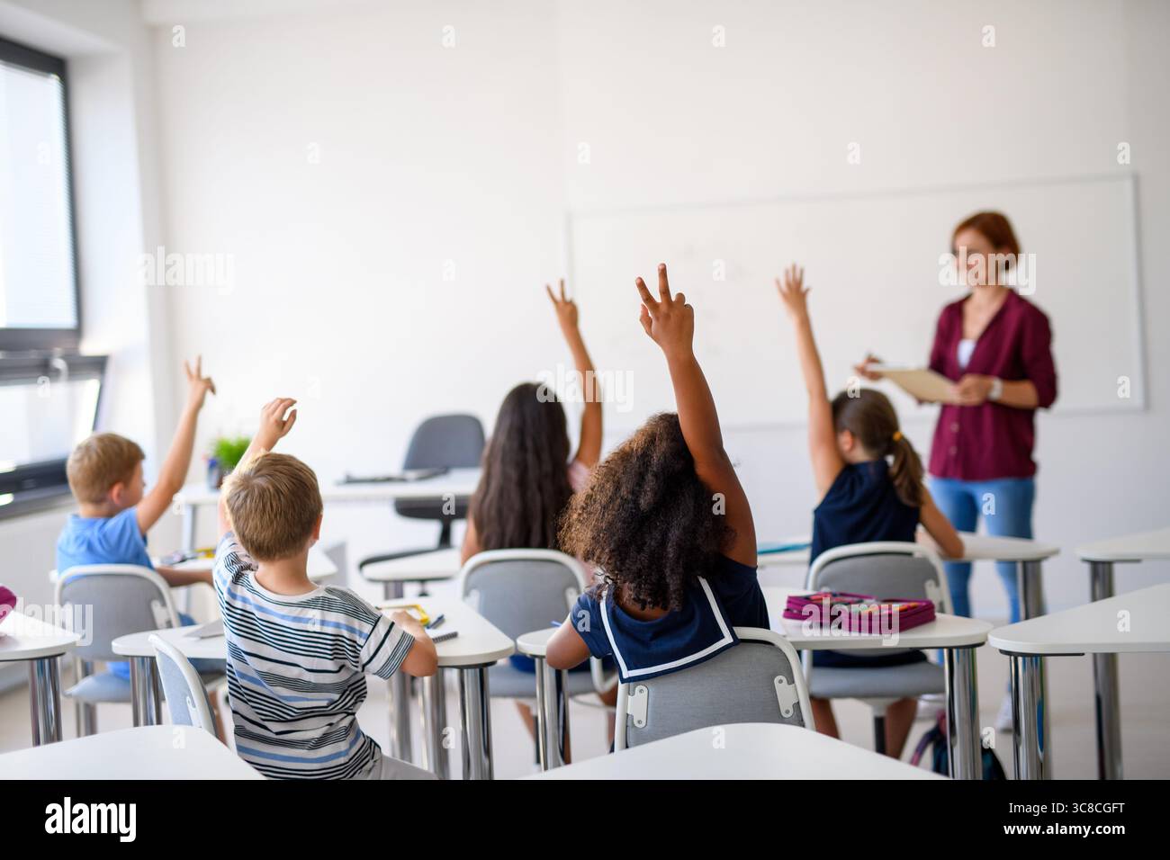 School children sitting at the desk in classroom on the lesson, raising ...