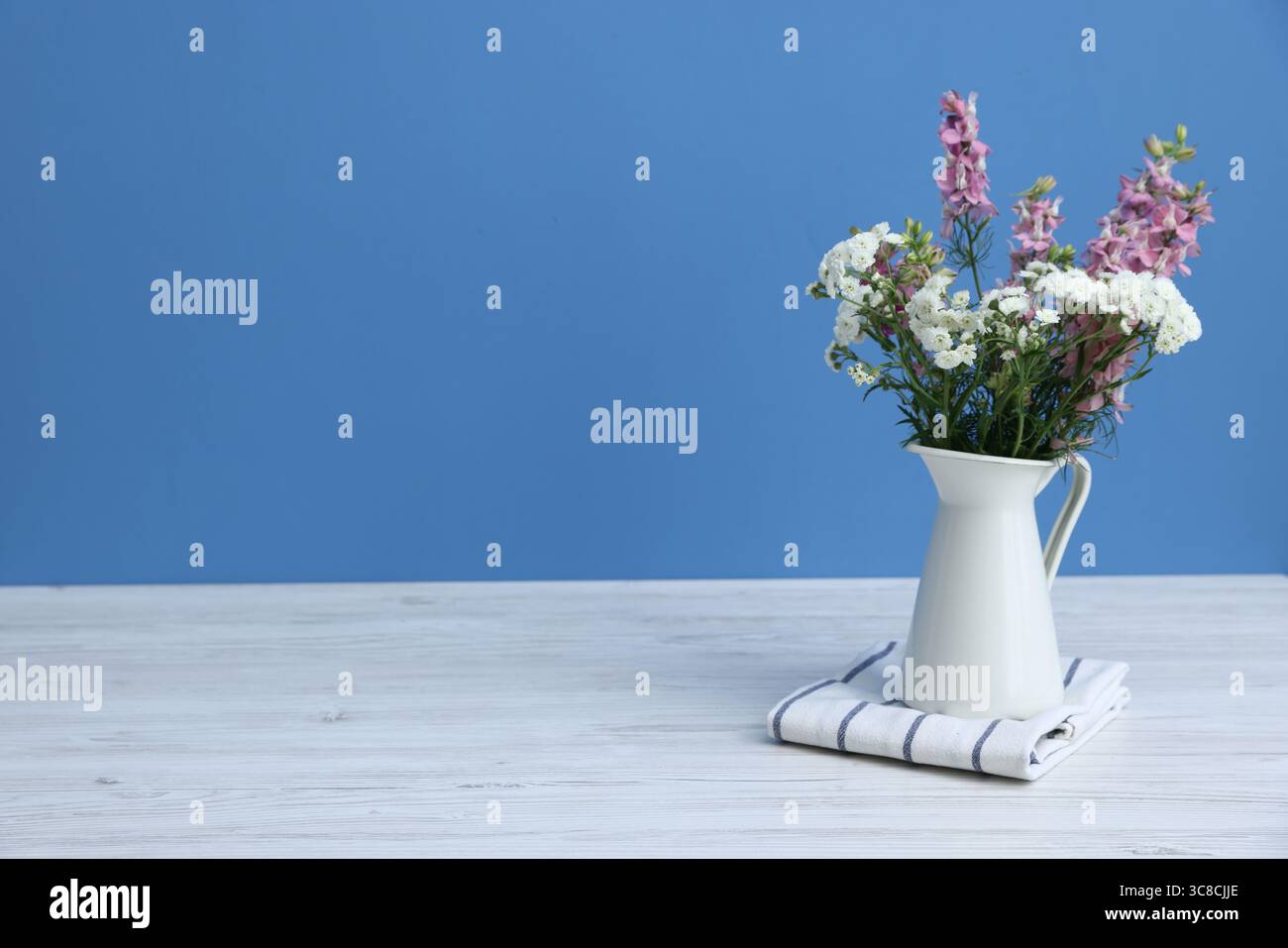 Beautiful flowers in vase on white wooden table against light blue ...