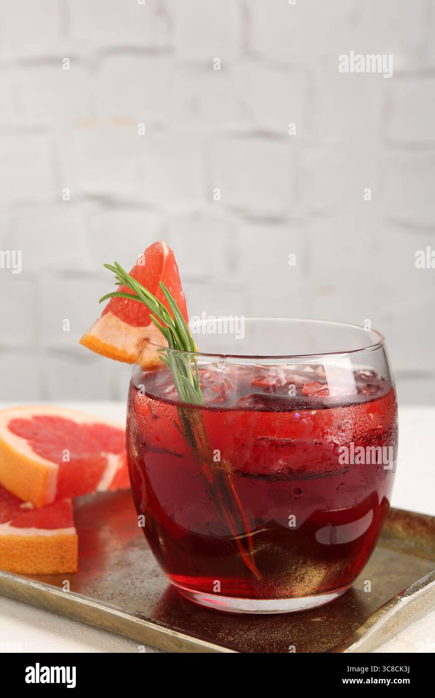 Tasty cocktail with grapefruit, ice cubes and rosemary on white table ...