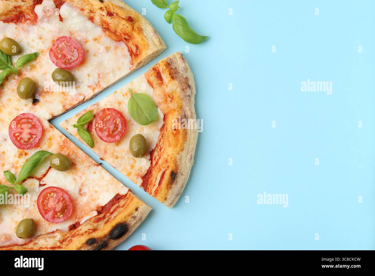 Delicious cut pizza with tomatoes, basil and olives on light blue ...