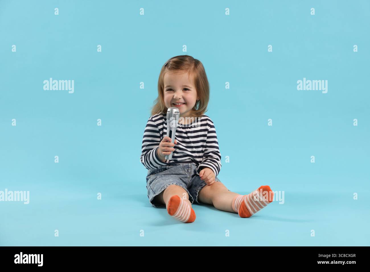 Cute little girl with microphone on light blue background Stock Photo ...