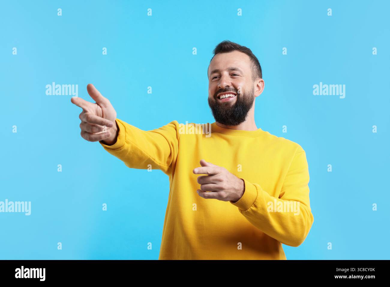 Handsome man pointing at something and laughing on light blue ...