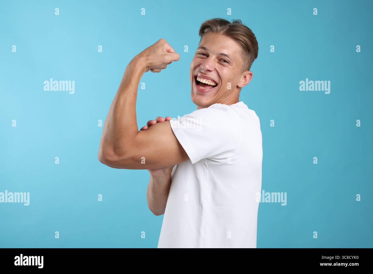 Strength. Happy man showing his biceps on light blue background Stock ...