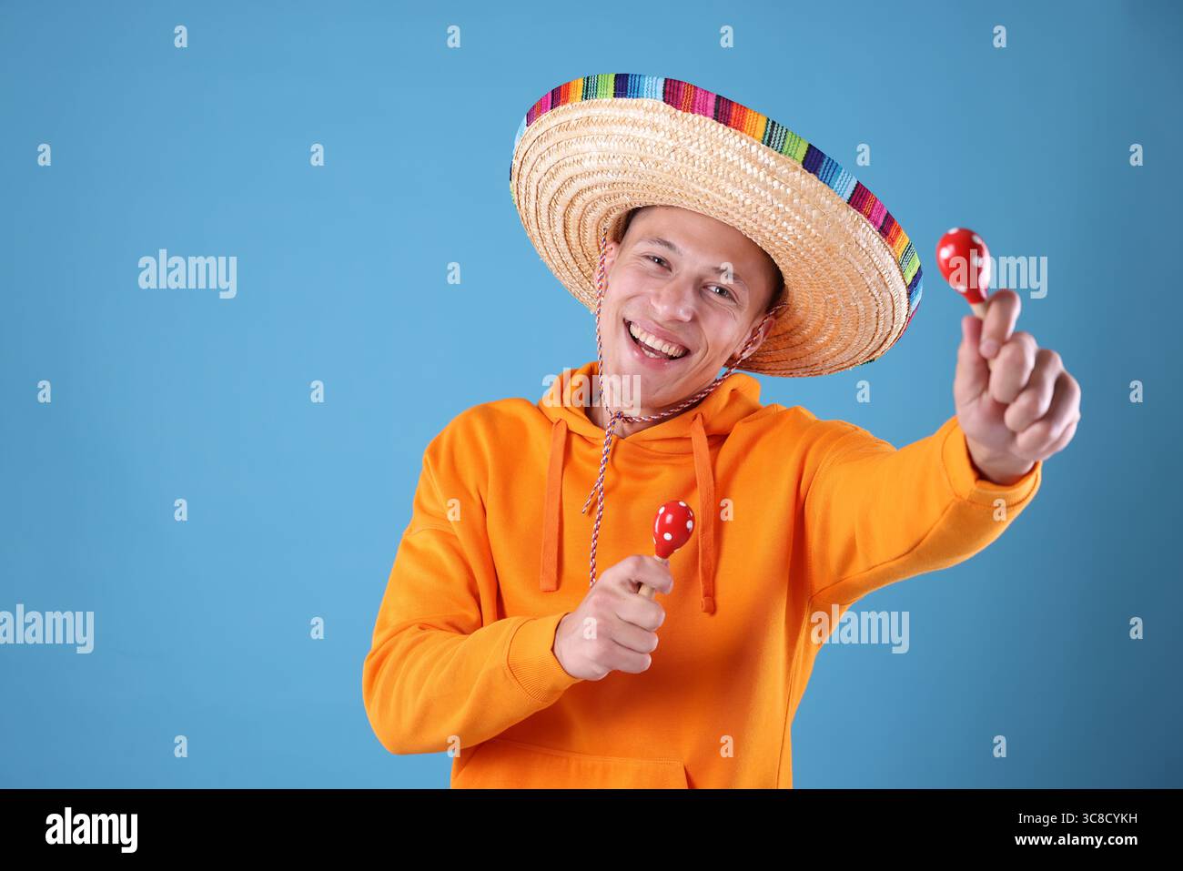 Happy man in sombrero hat playing maracas on light blue background ...