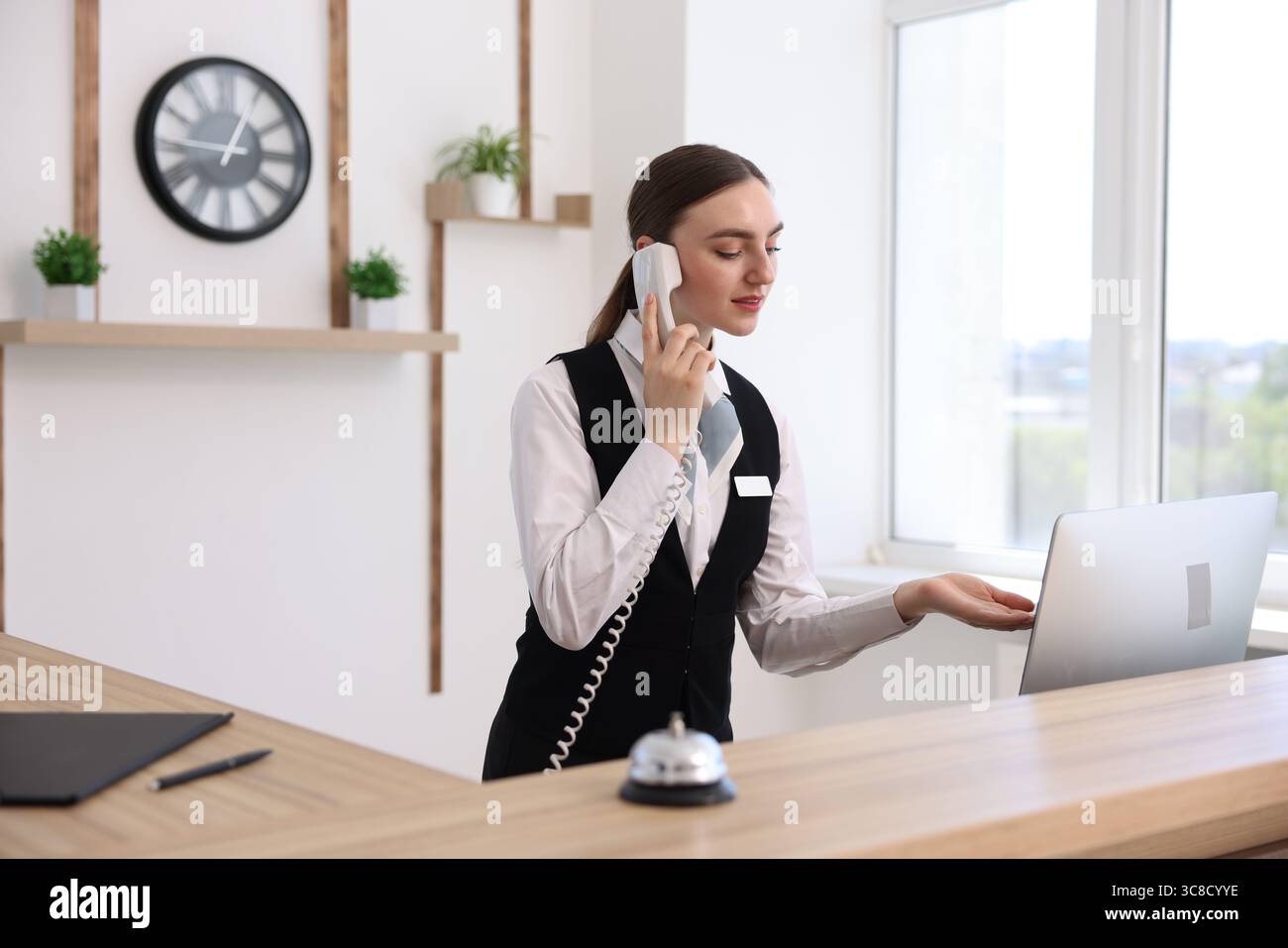 Receptionist talking with client by phone at reception desk in hotel ...