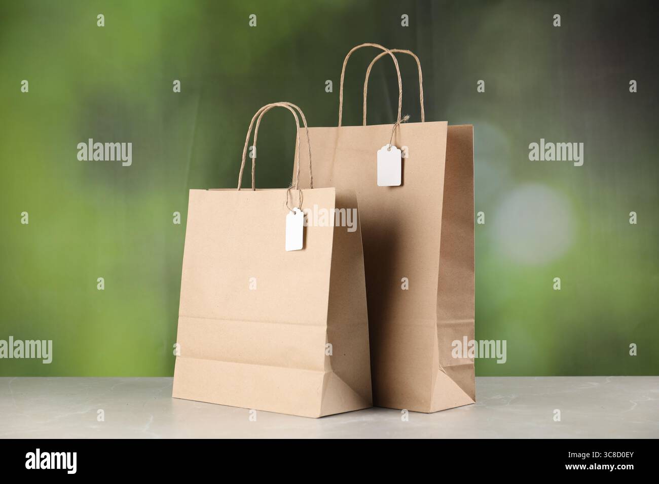 Kraft paper bags with blank labels on white table against blurred green ...
