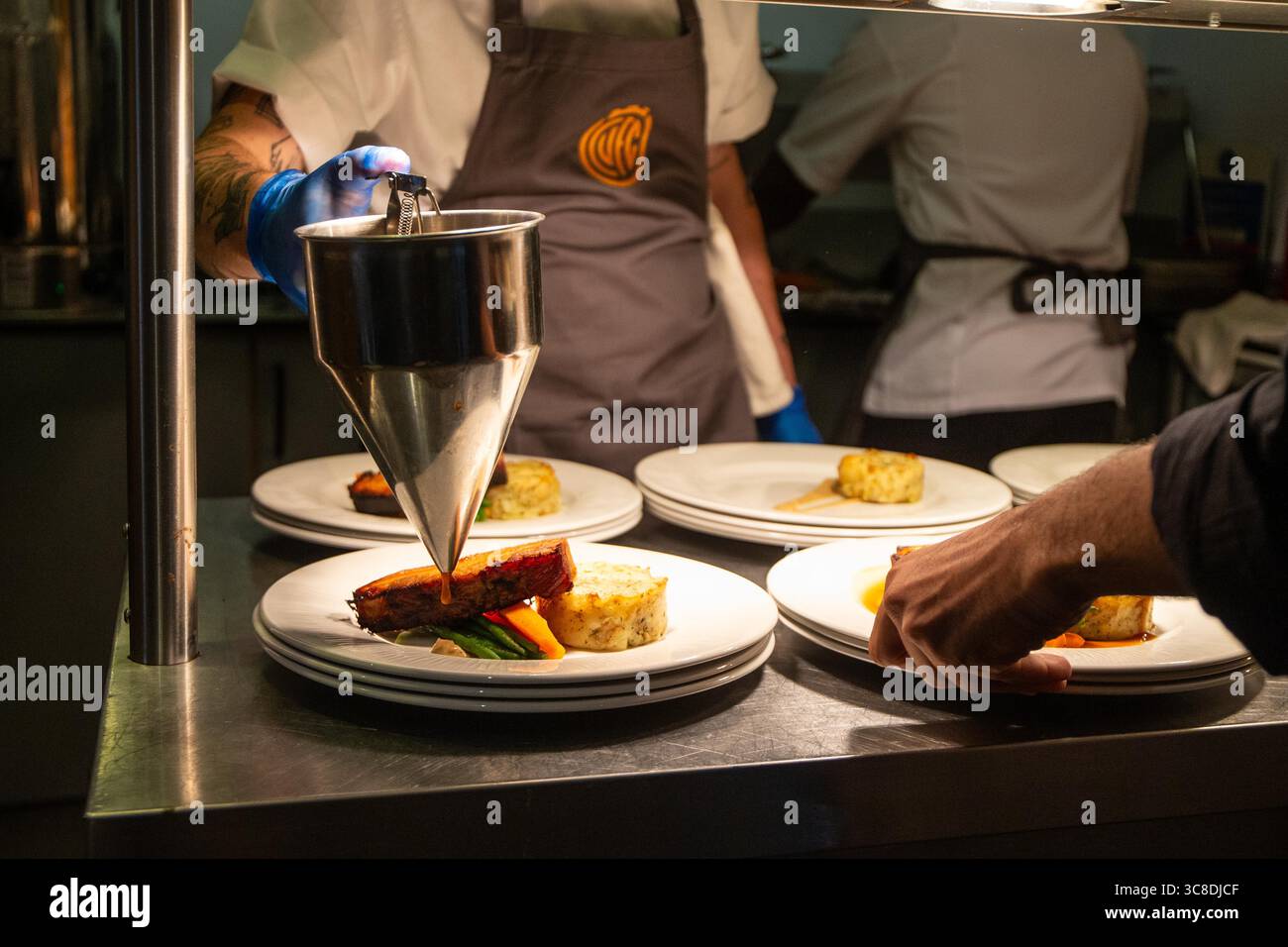 View of corporate catering hot food being prepared for service at football hospitality using gravy piston funnel. Stock Photo