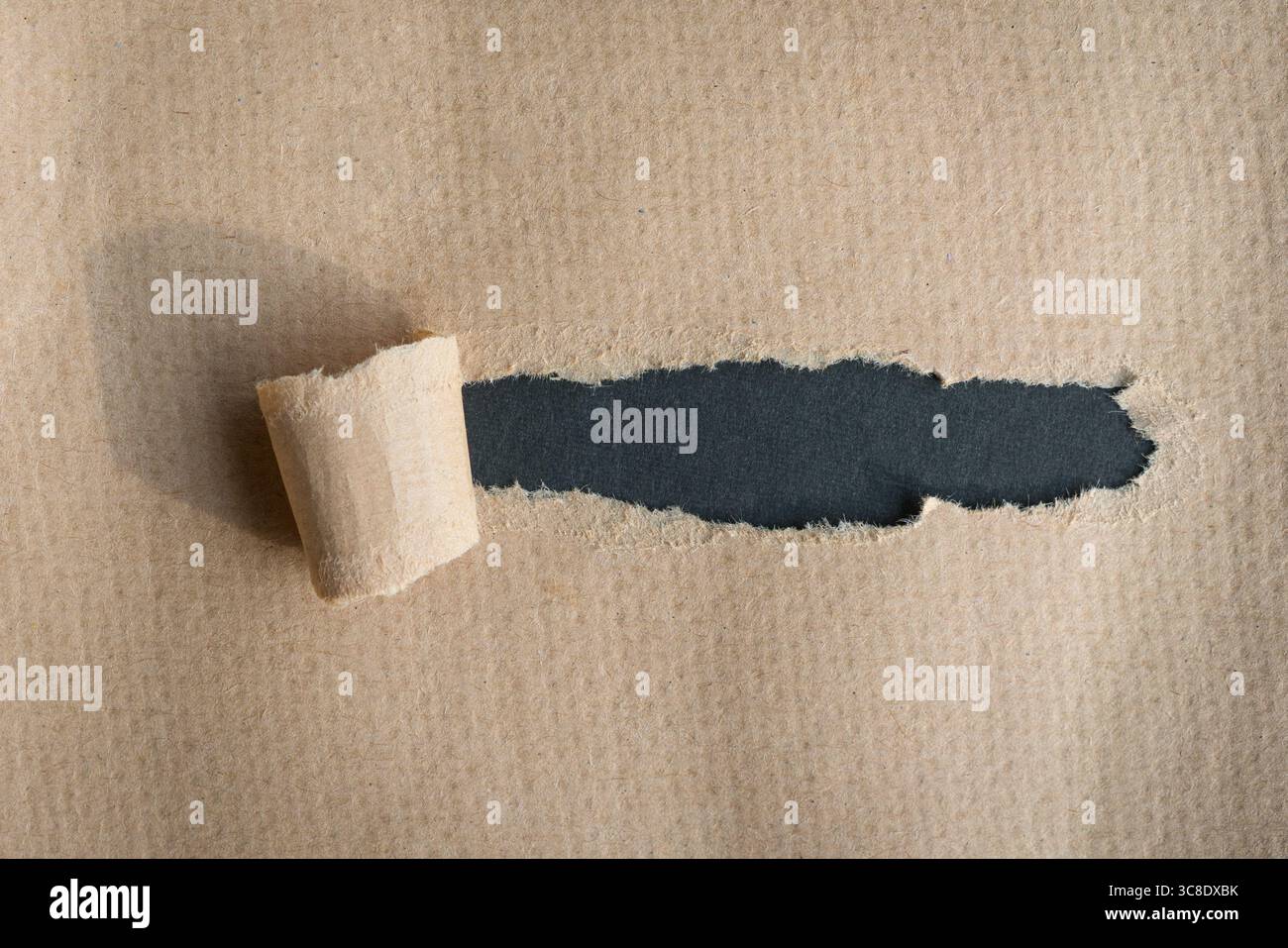 Hole ripped in brown textured paper on dark gray background. Copy space. Stock Photo