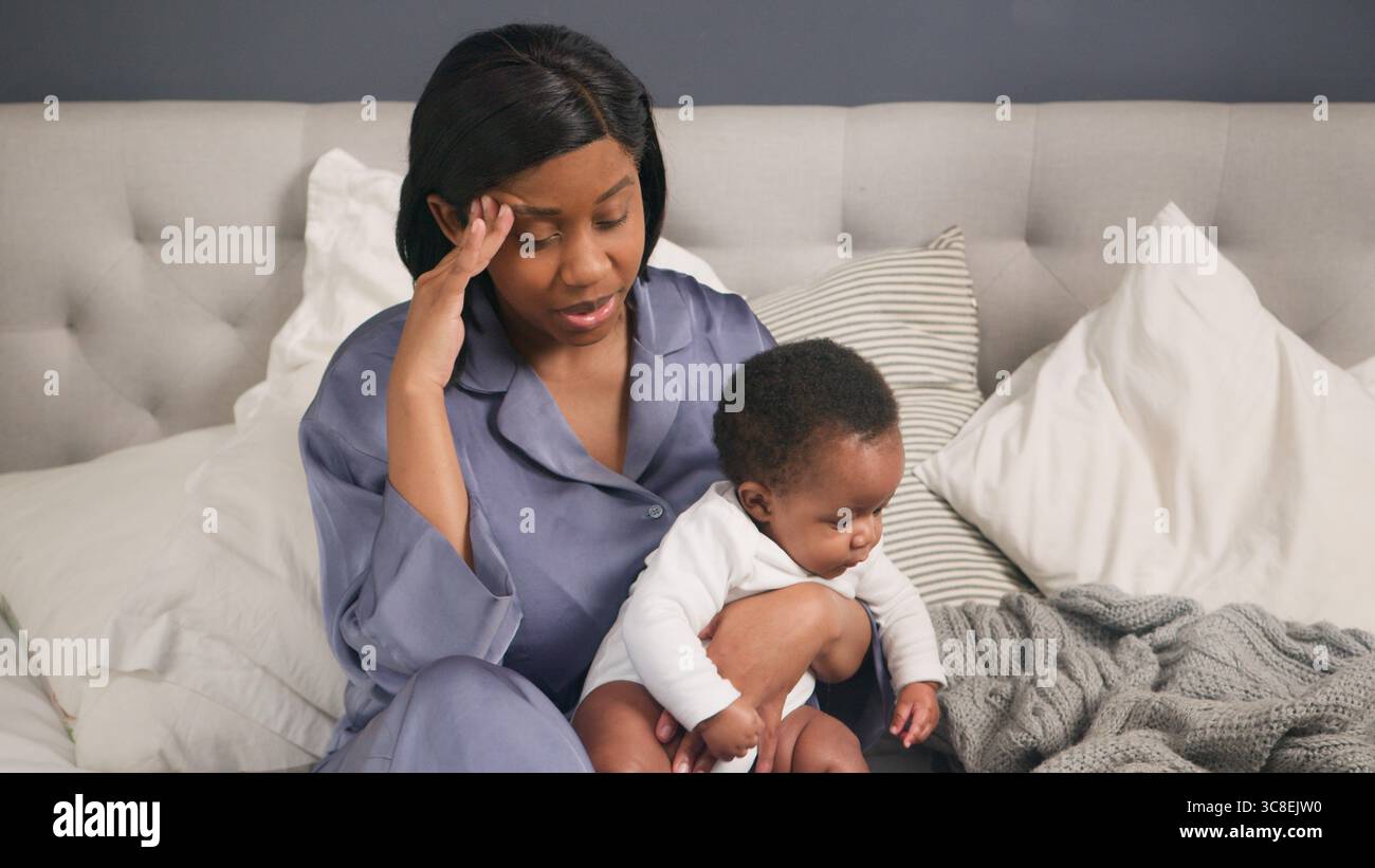 Postpartum Depression, Stressed Mother Sitting on Bed with Her Baby, Reflecting in an Emotional Moment Stock Photo