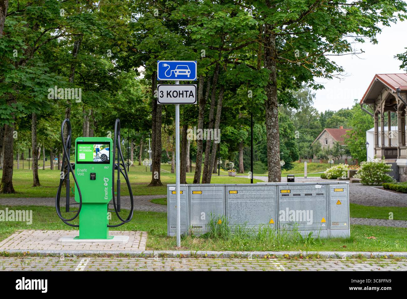 Public electric vehicle charging station with green charger in a park area in Estonia, marked with parking sign for three EV spots Stock Photo